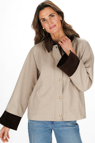 A woman modeling a beige button-front jacket with dark brown corduroy collar, cuffs, and front placket, paired with blue jeans against a plain white studio background.